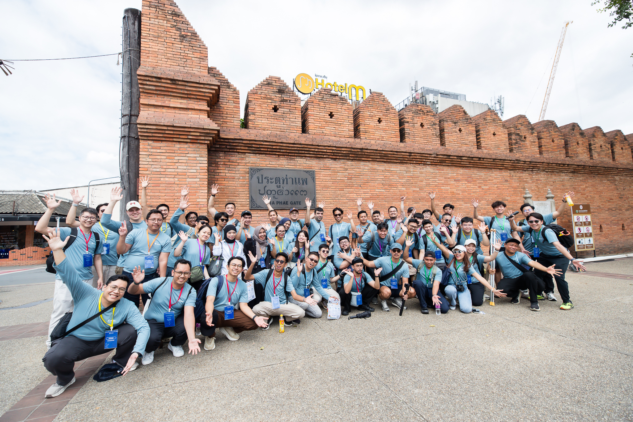 A retreat team of about 50 people waving at the camera in front of Tha Phae Gate in Chiang Mai
